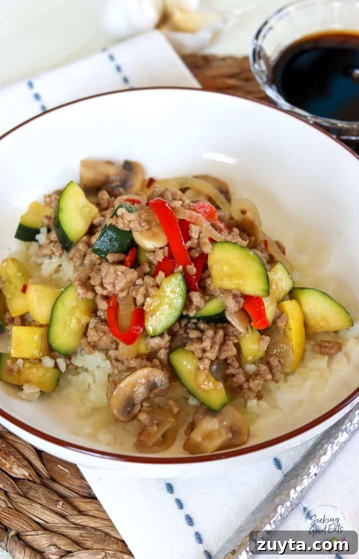 15-Minute Ground Pork Stir-Fry Recipe 2 A white bowl full of ground pork stir fry served over riced cauliflower.
