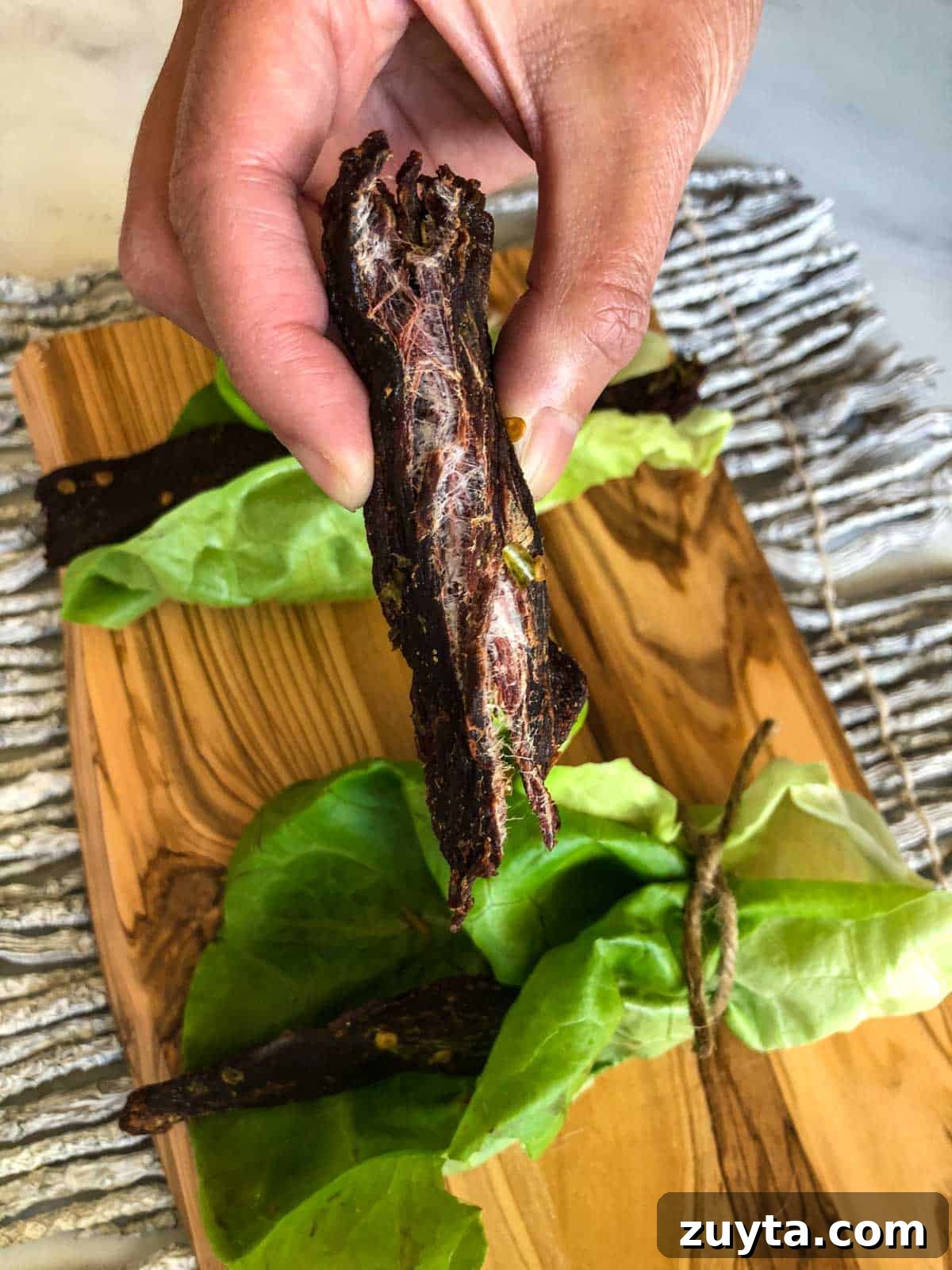 Homemade Asian-Spiced Venison Jerky Recipe 6 Deer jerky ripped in half showing it's finished with cutting board in background
