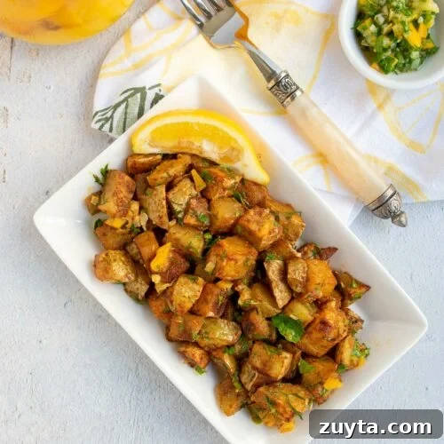Roasted harissa potatoes on a white plate with a small bowl of gremolata and a lemon napkin.
