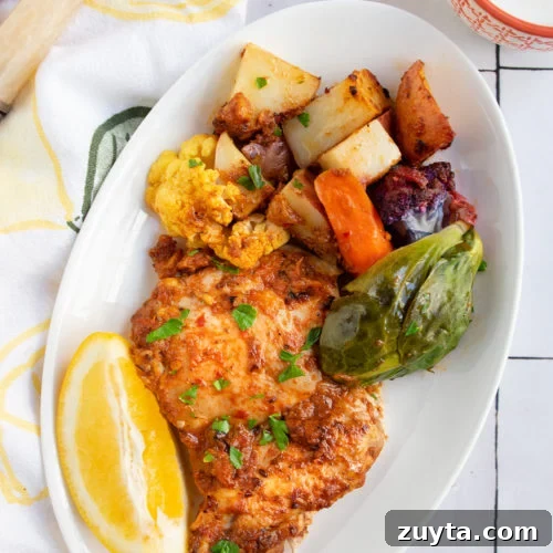 Harissa chicken and vegetables on a white plate with a slice of lemon.