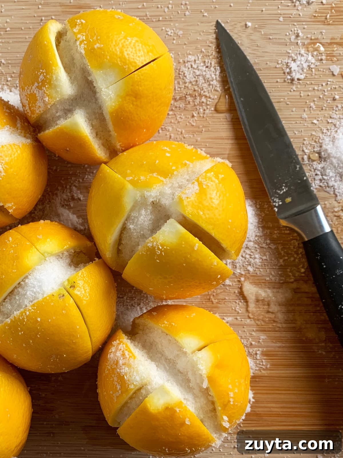 How to Make Preserved Lemons: Traditional Moroccan Recipe 3 Fresh lemons cut and filled with salt on a wooden cutting board with a knife next to it.