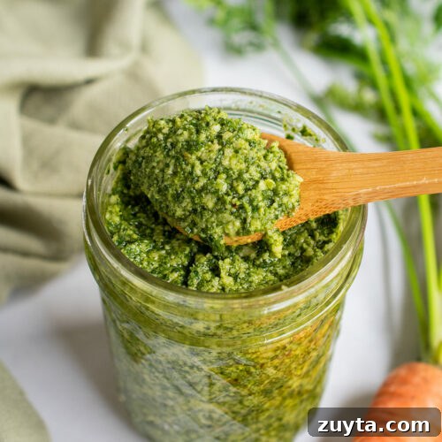 Preserved lemon pesto on a wooden spoon over a jar with carrot tops in the background.