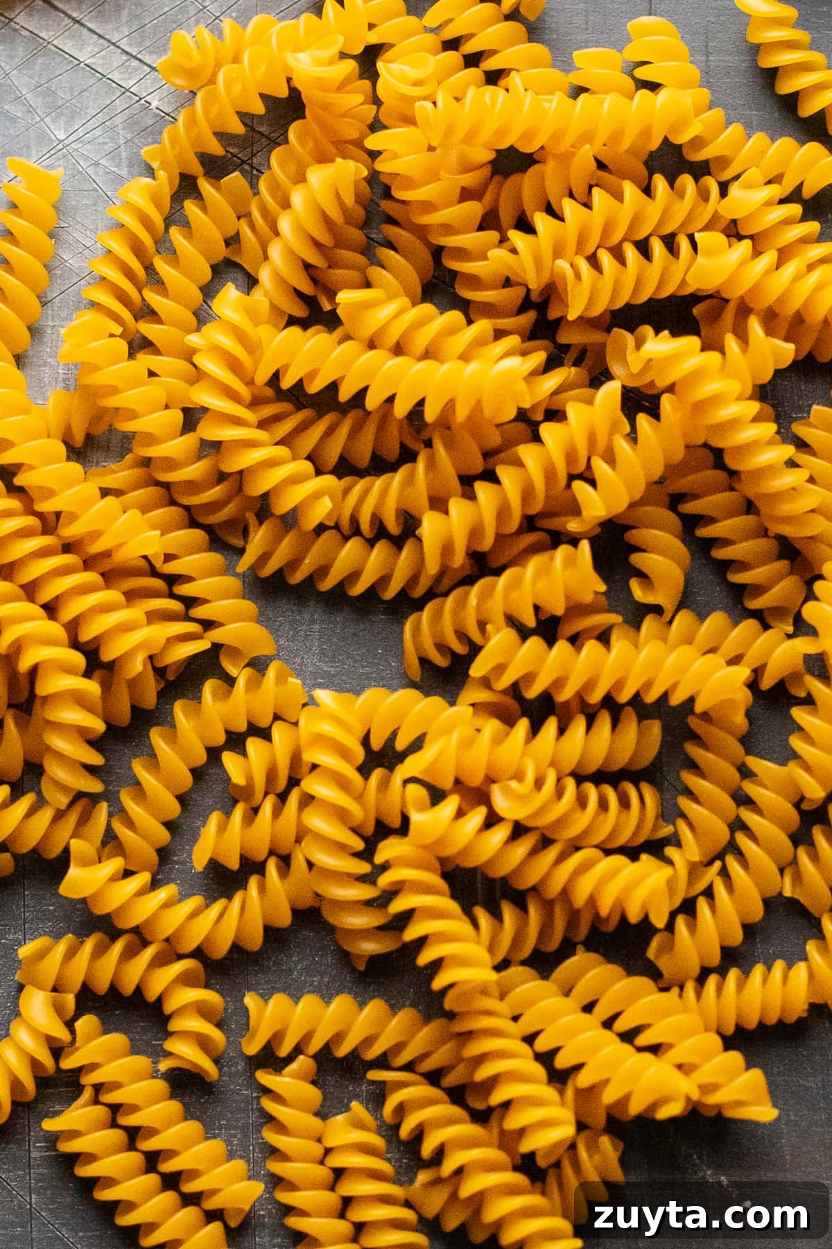 dry rotini pasta noodles arranged on gray background.
