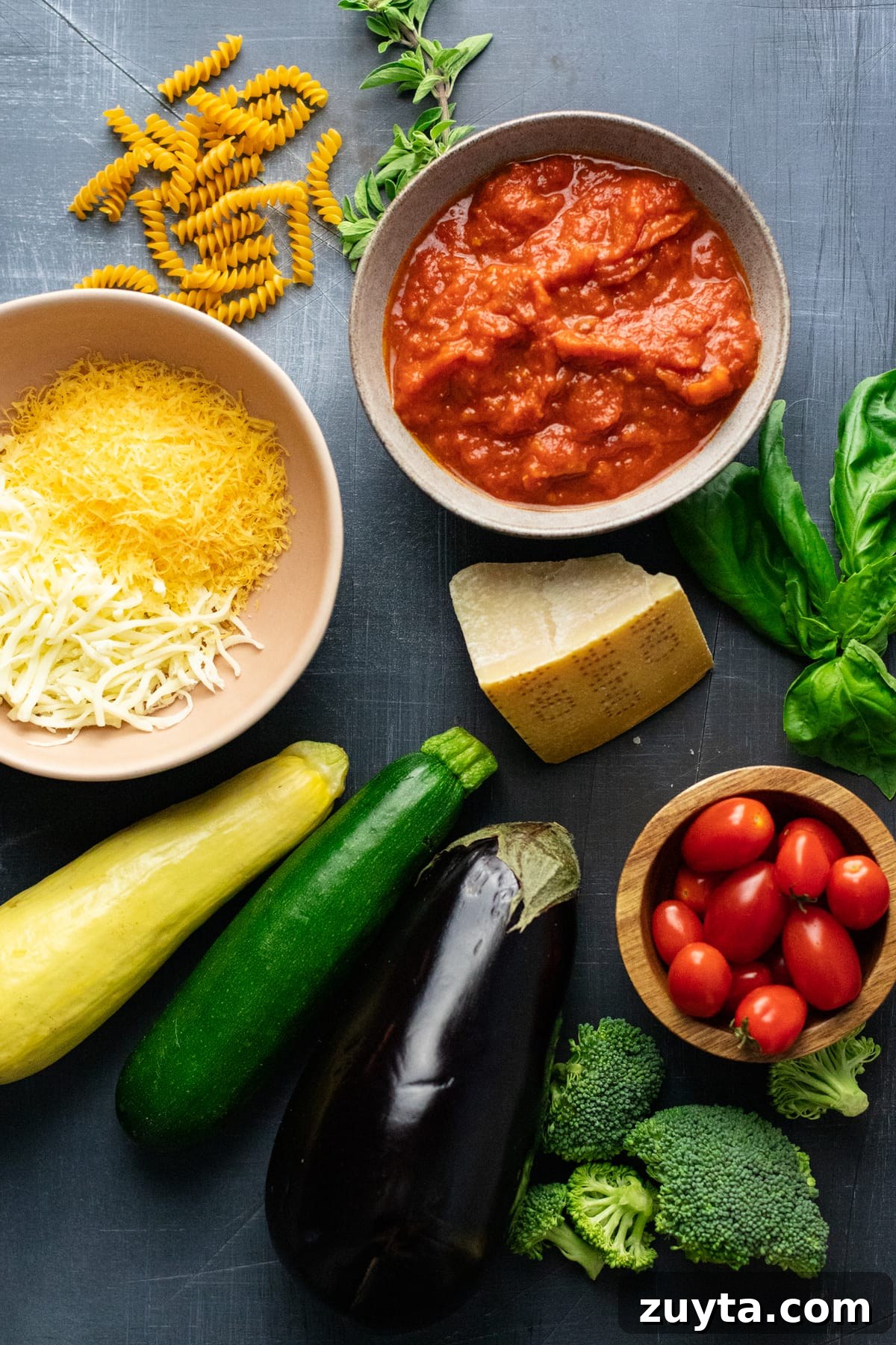ingredients for rotini pasta and vegetables arranged on dark gray background.