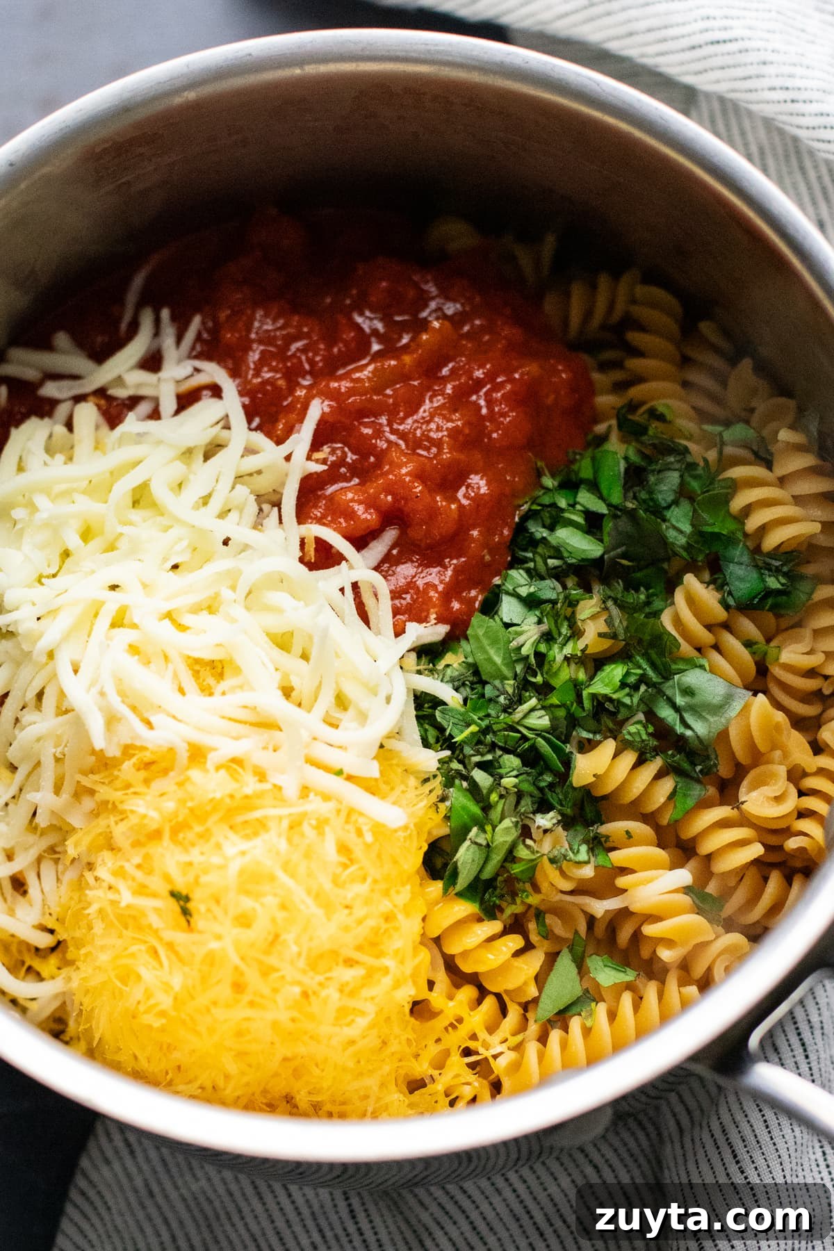 a pot with cheese, red tomato sauce, fresh herbs, and rotini pasta in it.