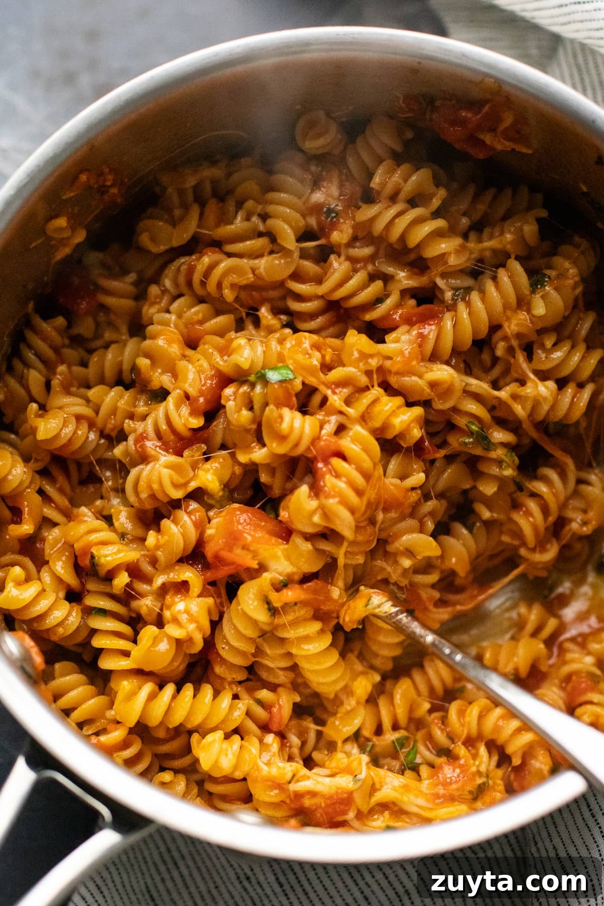 rotini pasta noodles being mixed in a pot with sauce and melted cheese.