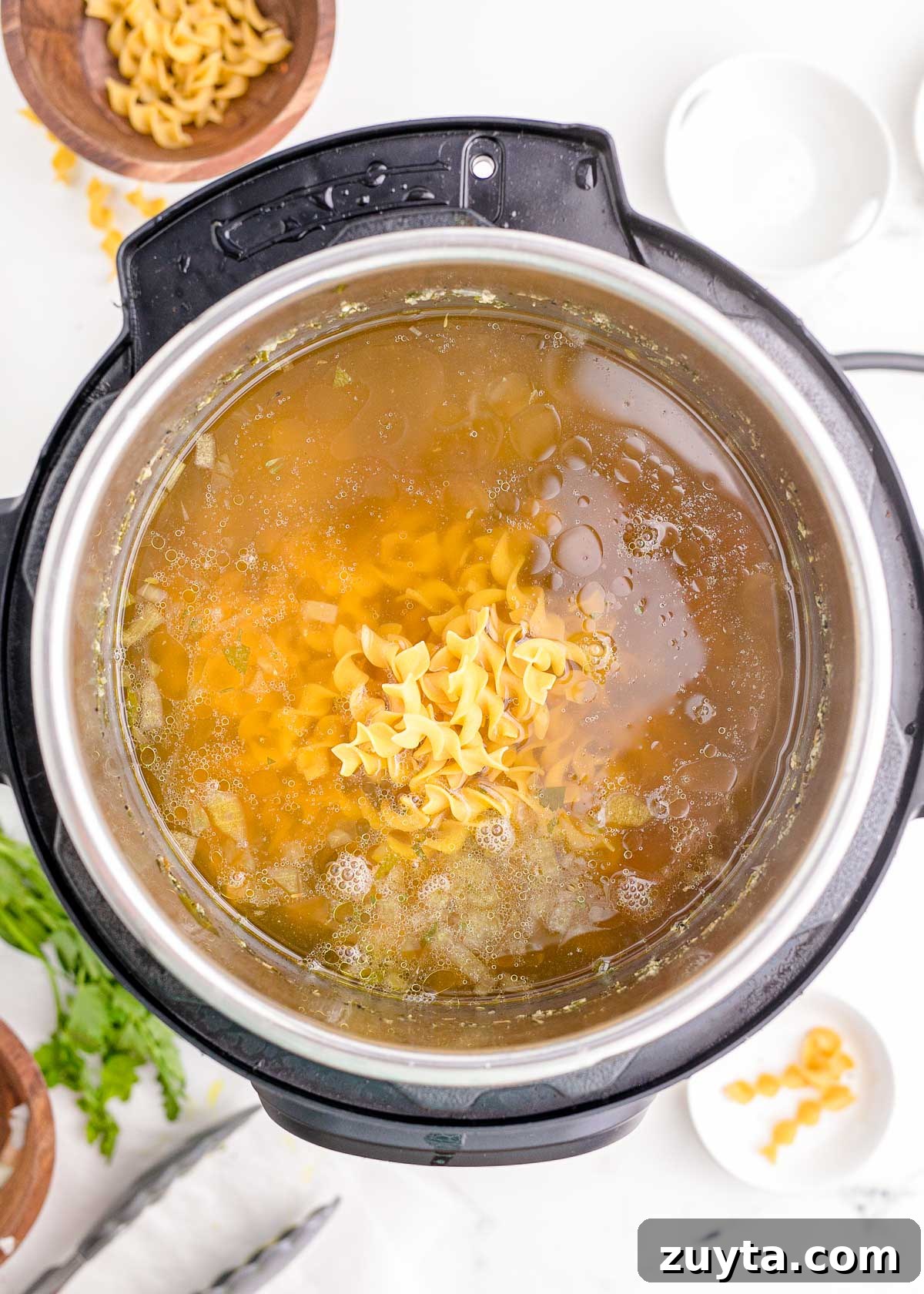 Egg noodles being added to an instant pot to make chicken noodle soup.