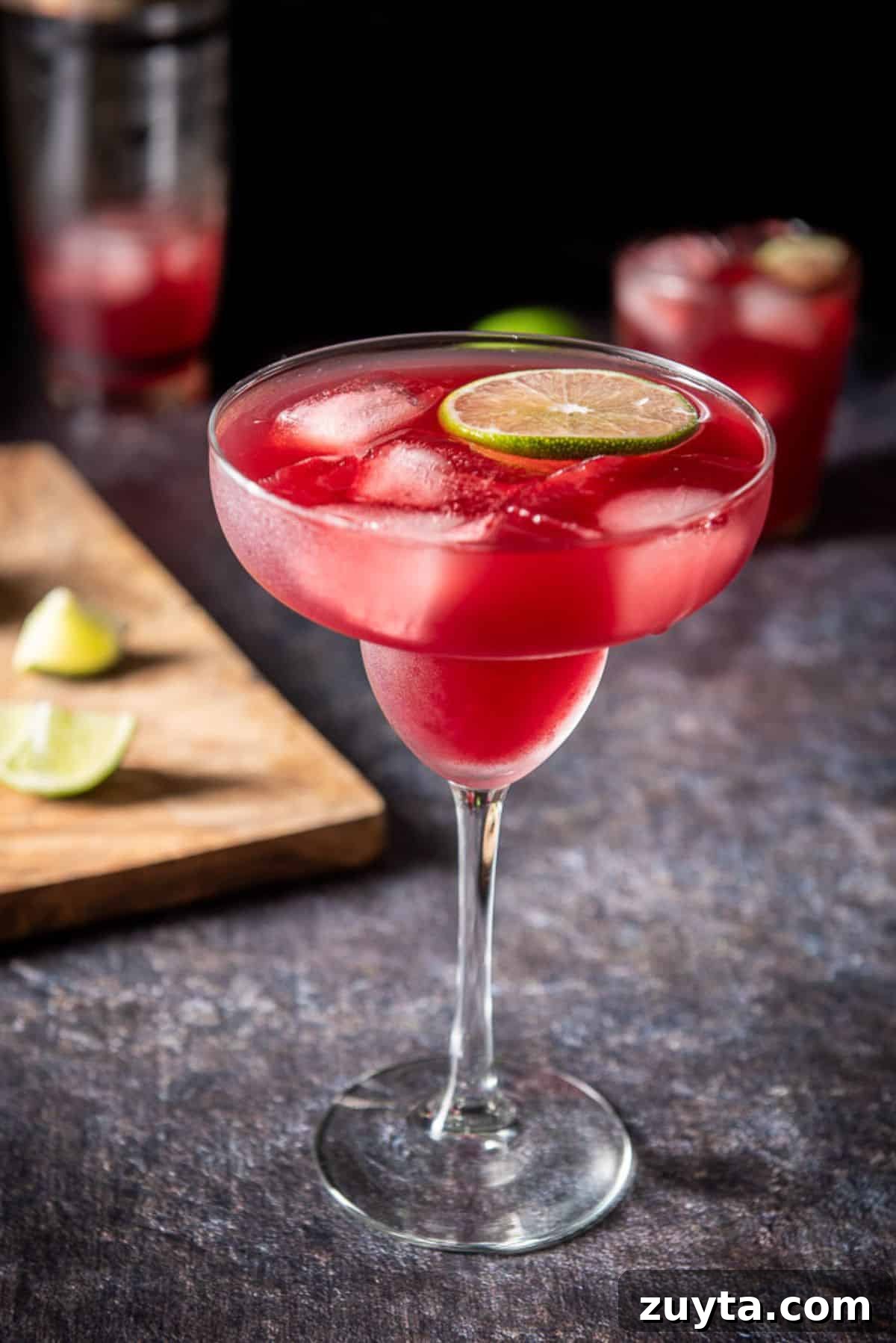 Pomegranate Margarita Cocktail Recipe 5 Classic margarita glass in front with liquid in it along with a floating lime wheel and ice