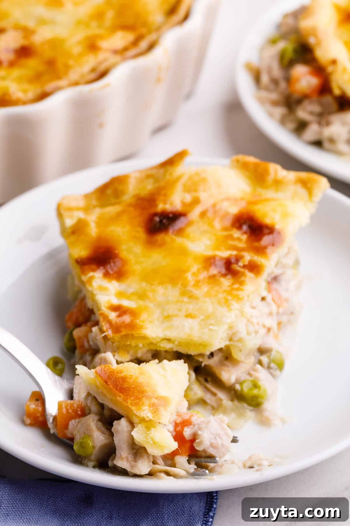 slice of turkey pot pie with a forkful of pie served on a white round plate.