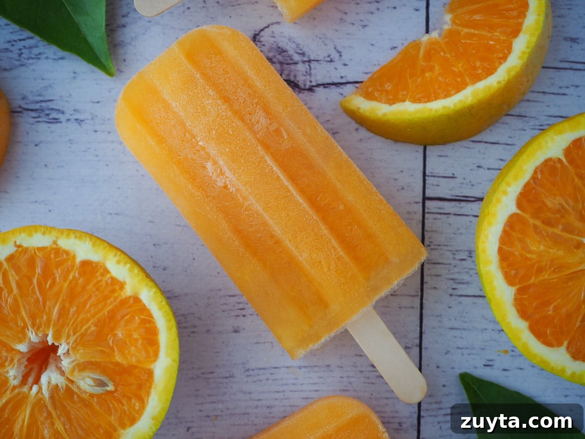 Homemade Orange Popsicles Recipe 2 Orange popsicle on a diagonal, with fresh oranges and orange leaves.