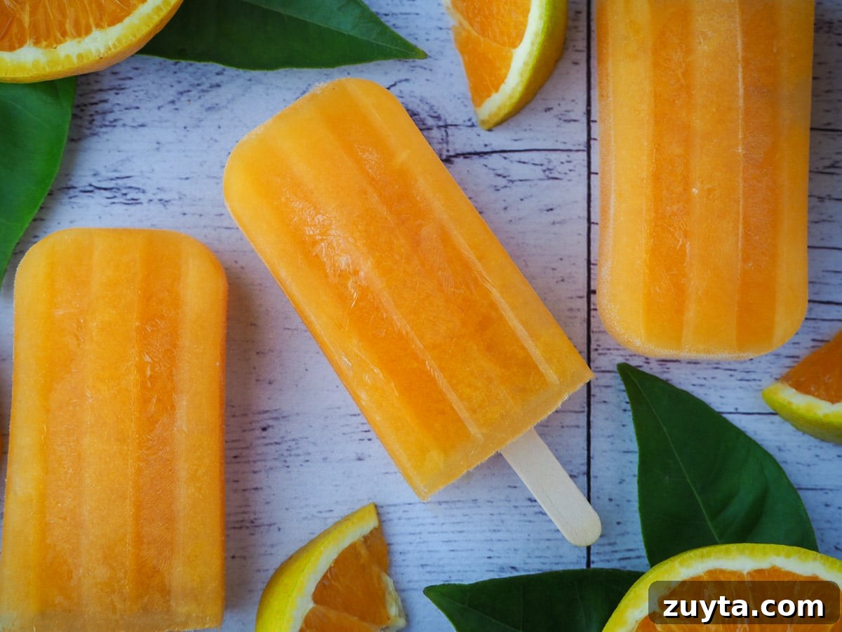 Homemade Orange Popsicles Recipe 8 Orange popsicles with fresh oranges and orange leaves.