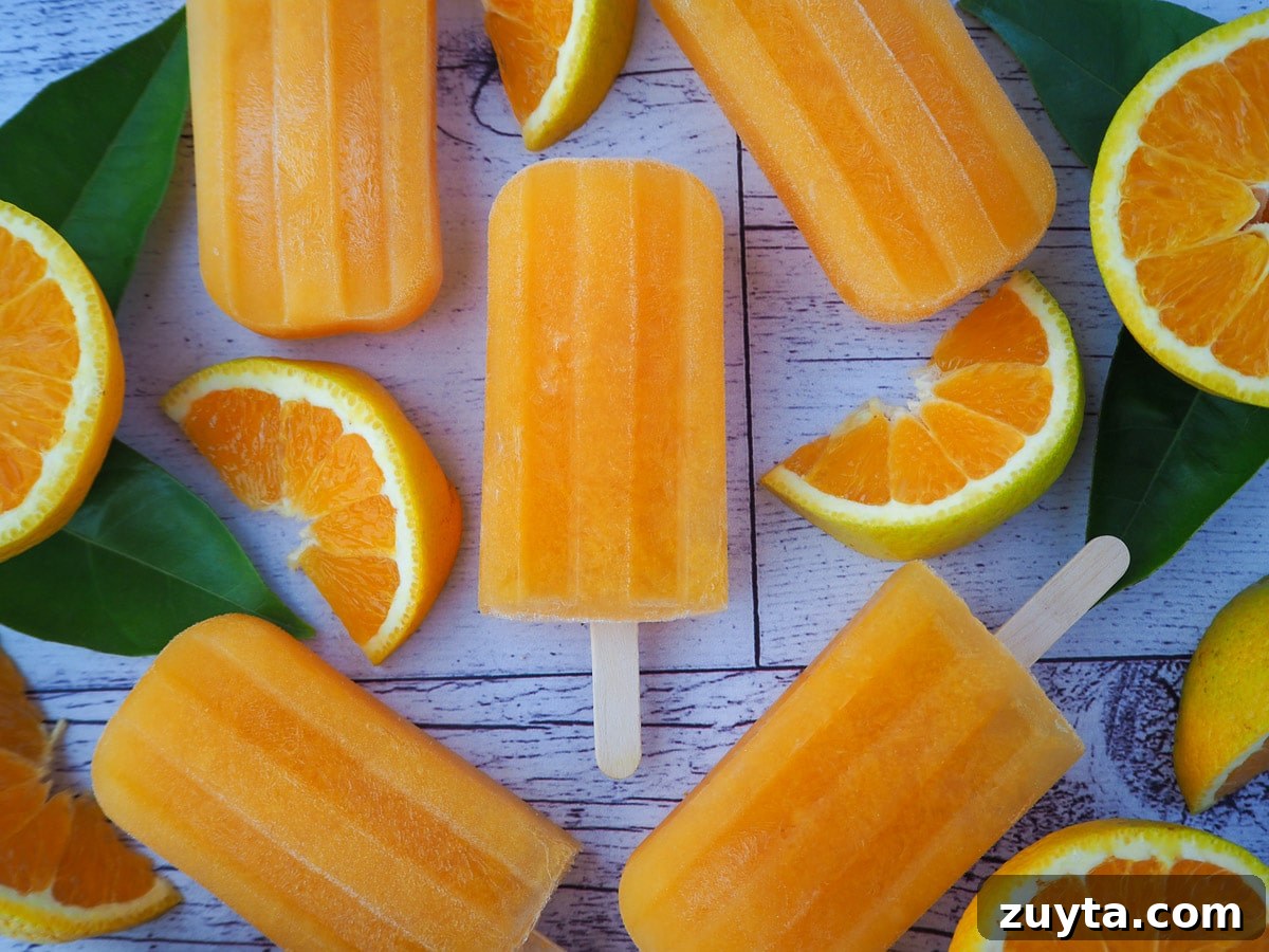 Homemade Orange Popsicles Recipe 9 Orange popsicles with fresh orange and orange leaves.