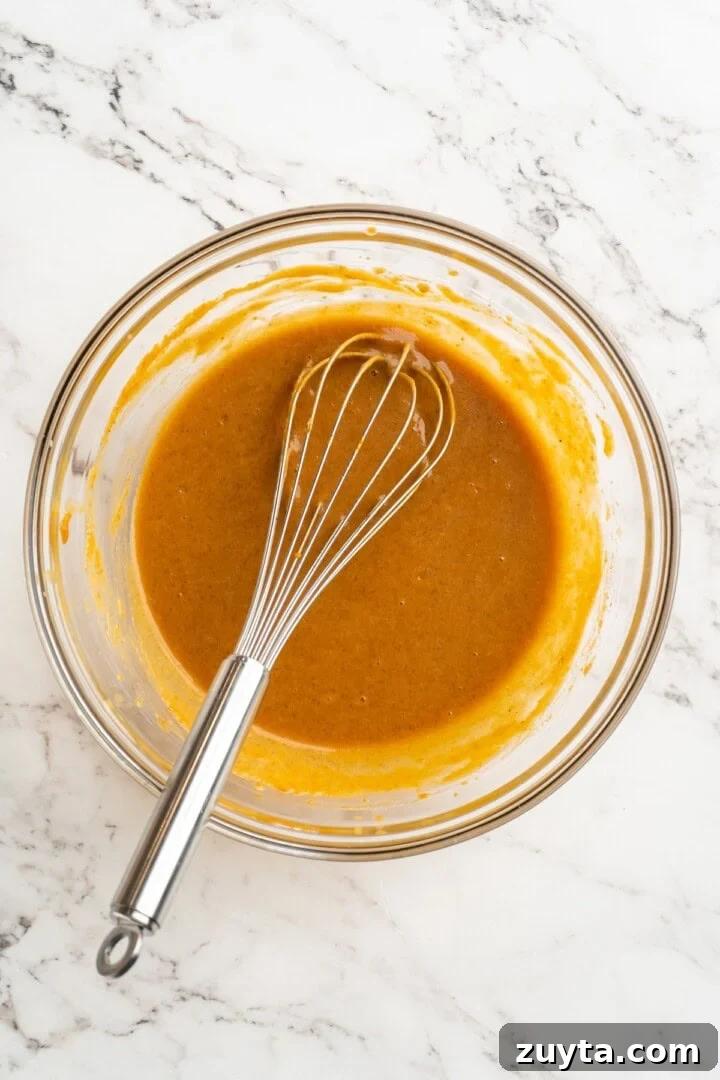 Mix wet ingredients. Overhead view of wet ingredients for pumpkin bread in bowl with whisk