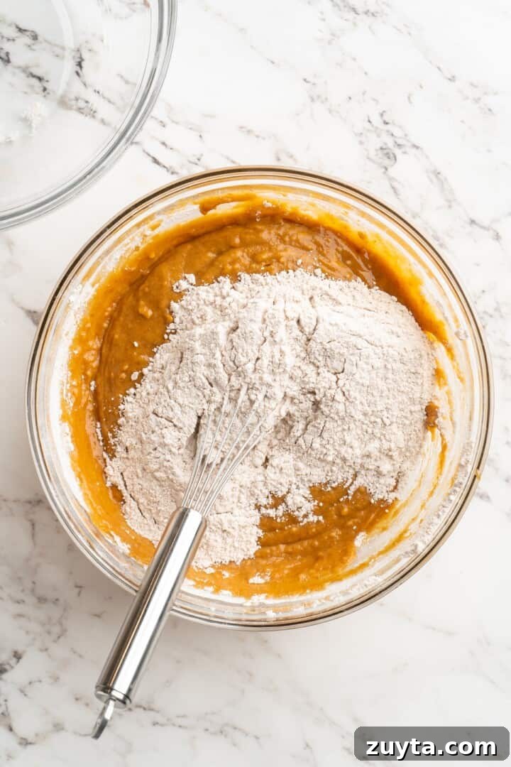 Add dry to wet. Overhead view of dry ingredients added to bowl of wet ingredients for pumpkin bread