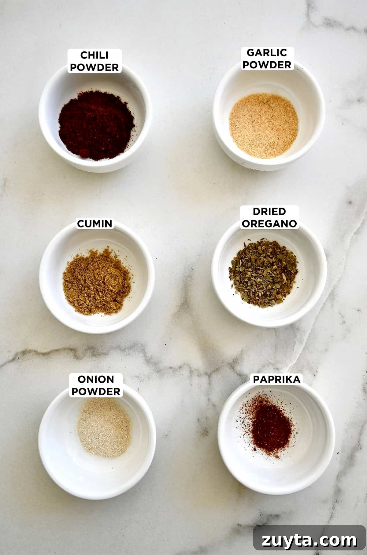 Homemade Taco Seasoning Mix Recipe 2 Six small bowls containing taco seasoning ingredients, including chili powder, ground cumin, onion powder, paprika, dried oregano and garlic powder.