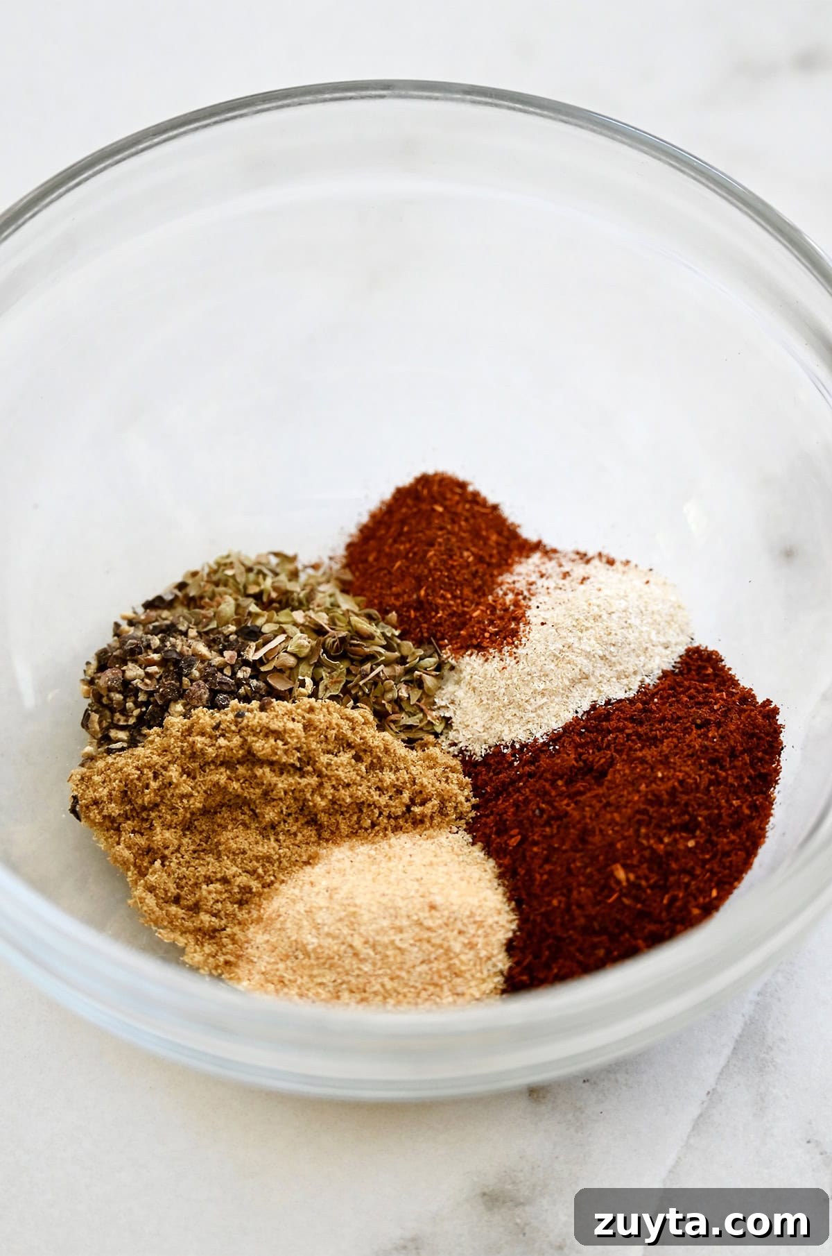 Homemade Taco Seasoning Mix Recipe 3 A glass bowl containing garlic powder, garlic onion, chili powder, ground cumin, black pepper, dried oregano and paprika