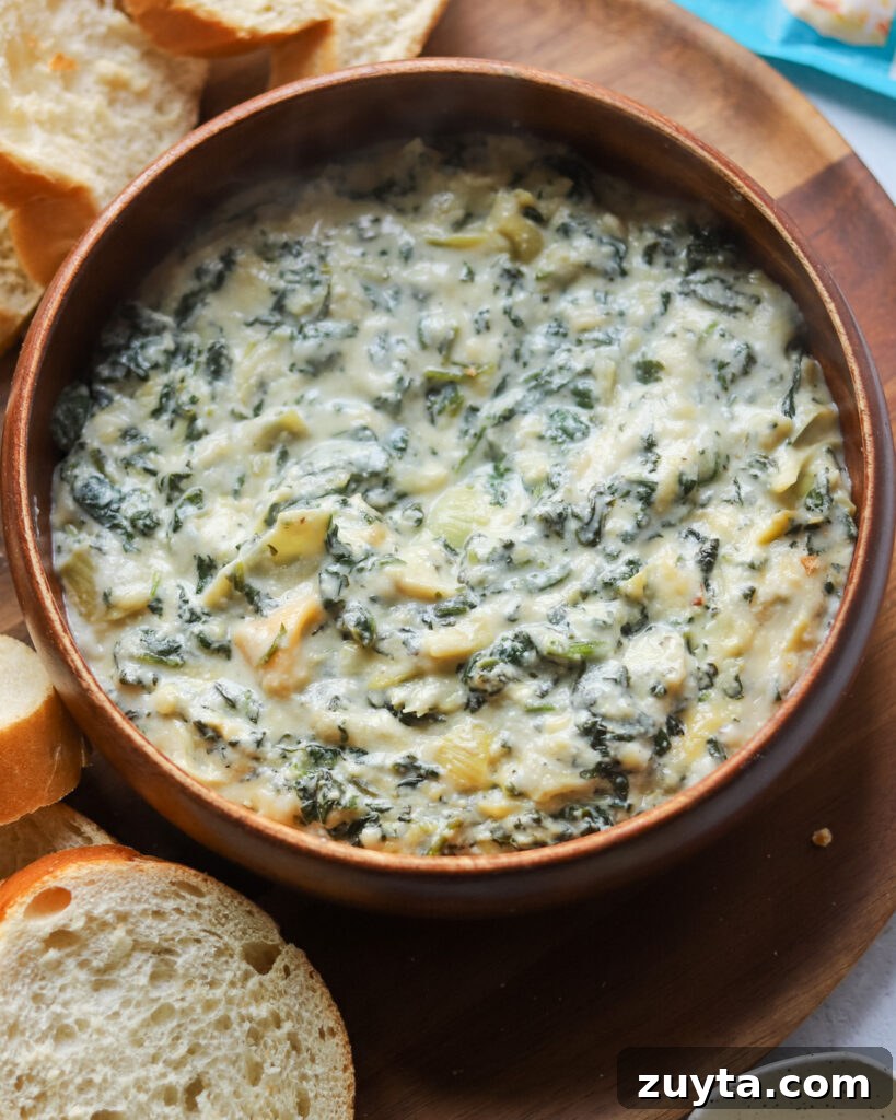 Creamy Vegan Spinach and Artichoke Dip with Silken Tofu 3 overhead view of a wooden bowl with homemade vegan spinach artichoke dip next to sliced bread.