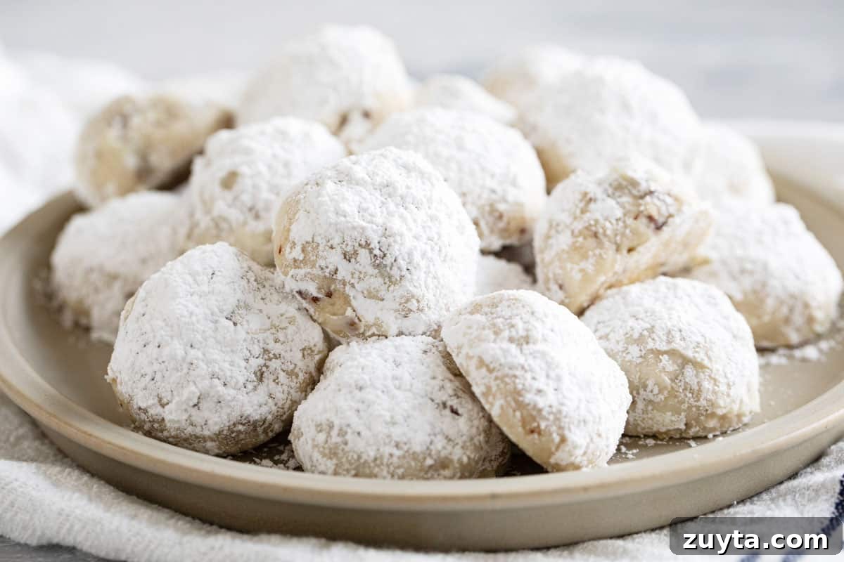 Mexican wedding cookies covered in powdered sugar, on a plate.