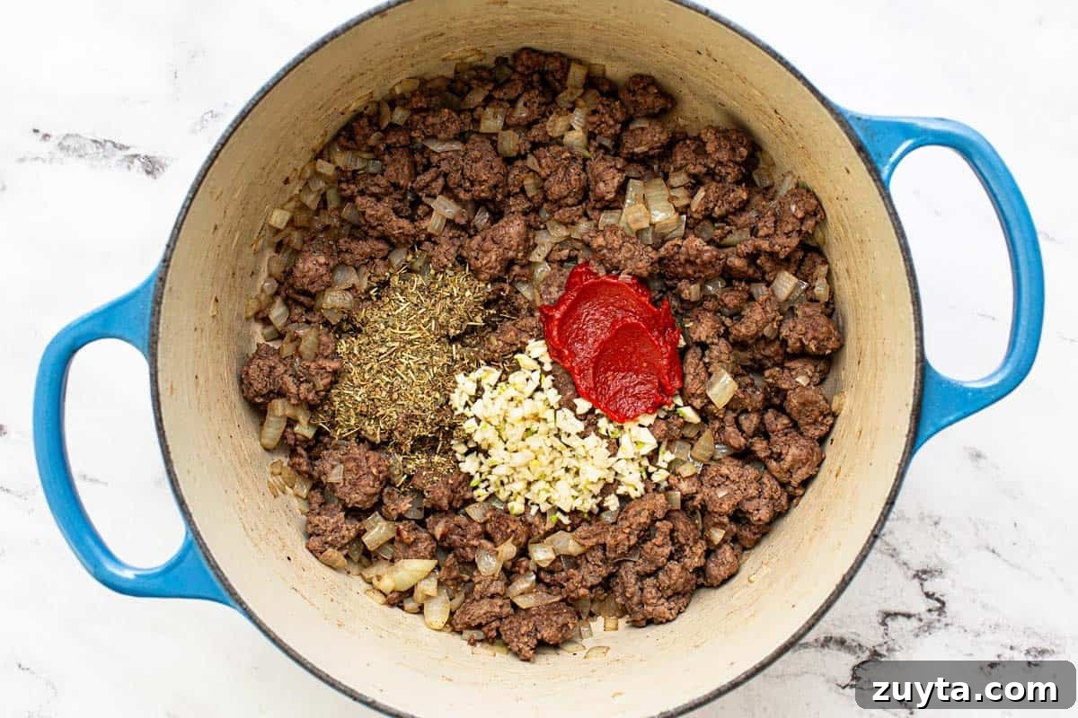 Weeknight One-Pot Ground Beef Stew Recipe 4 Ground beef in a large pot with herbs, garlic, and tomato paste.