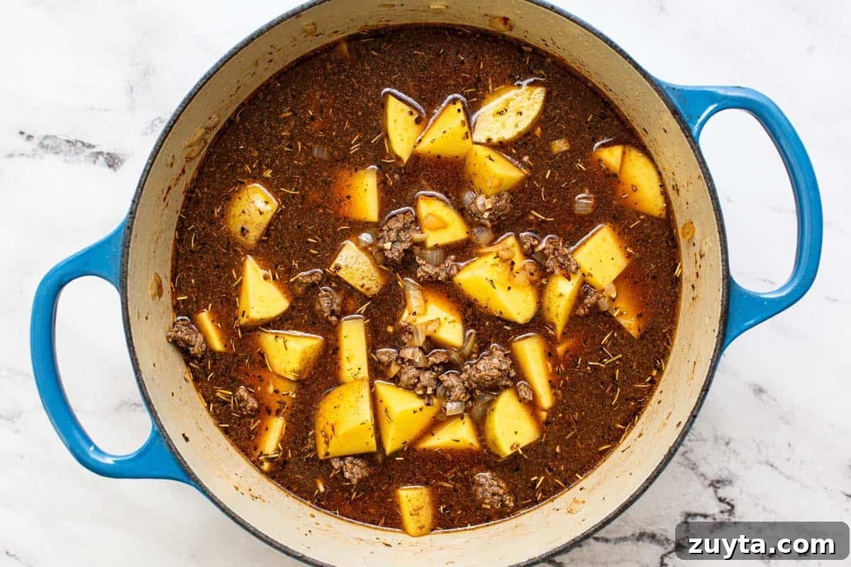Weeknight One-Pot Ground Beef Stew Recipe 5 Potatoes and ground beef in broth in a large pot.