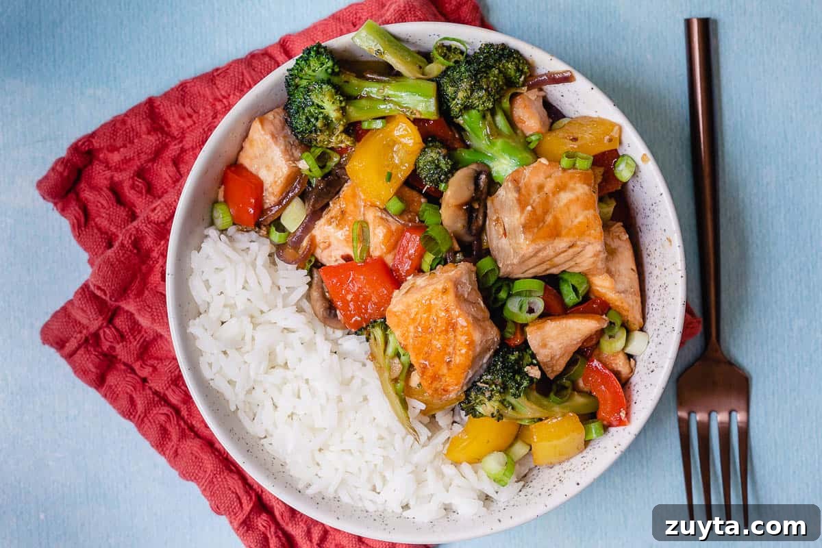 Soy-Ginger Salmon Stir-Fry with Vegetables 11 bowl of stir fry salmon with vegetables and white rice next to fork and red napkin.