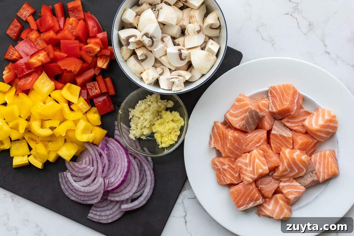 Soy-Ginger Salmon Stir-Fry with Vegetables 6 plate with cubed salmon next to cutting board with chopped peppers, mushrooms, onions, garlic, and ginger.
