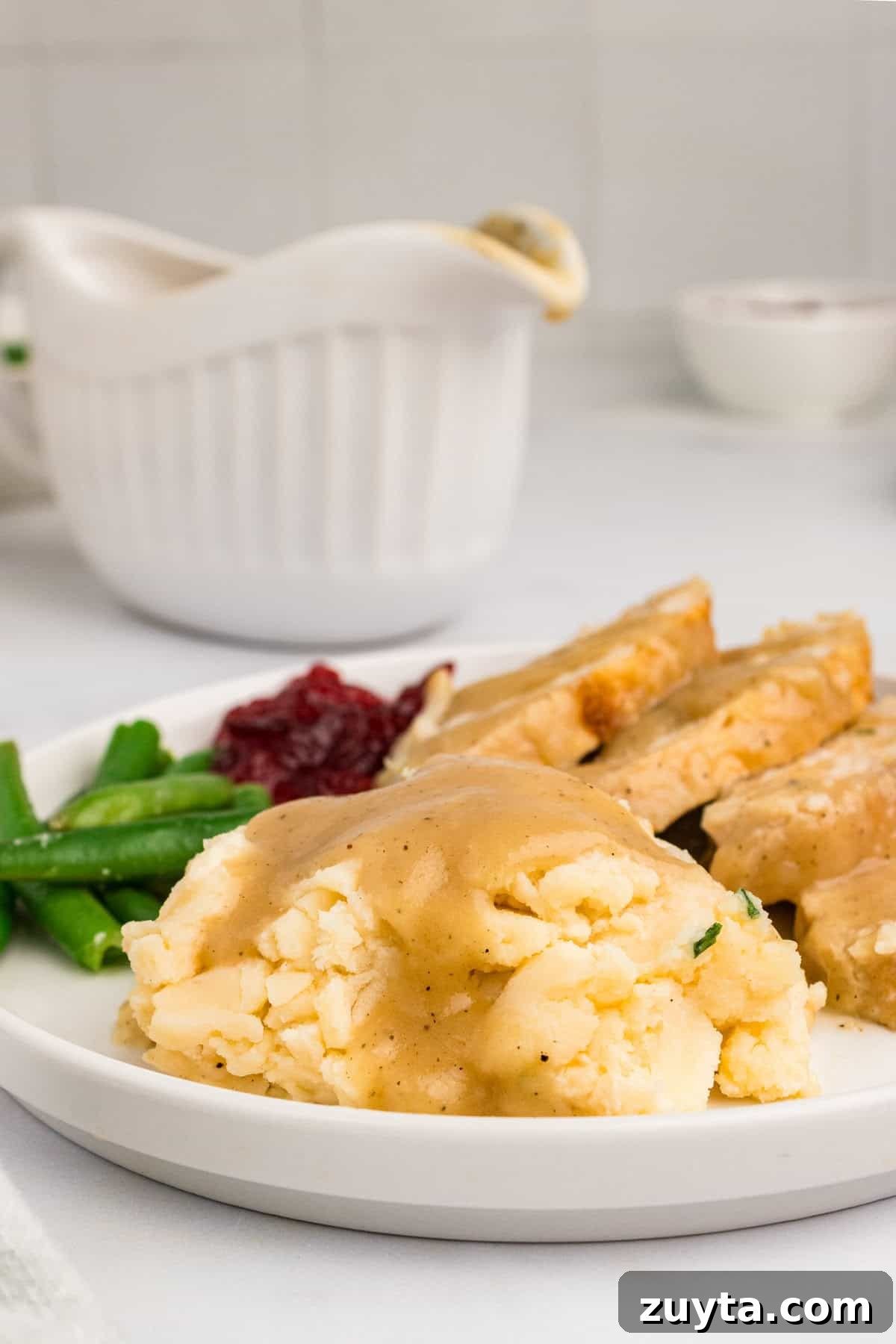 How to Make Turkey Gravy Without Drippings 11 Thanksgiving dinner: mashed potatoes and gravy, sliced turkey with gravy, mashed potatoes, cranberry sauce, and a gravy boat in the background.