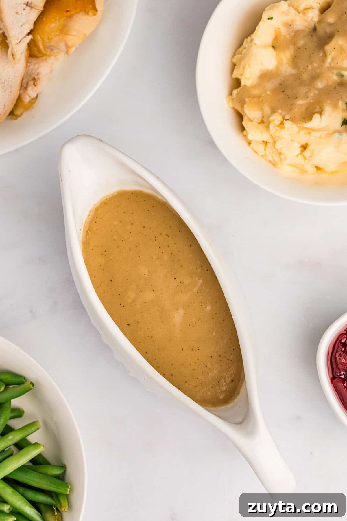 How to Make Turkey Gravy Without Drippings 9 Easy turkey gravy without drippings in gravy boat with green beans, turkey, and mashed potatoes around it.