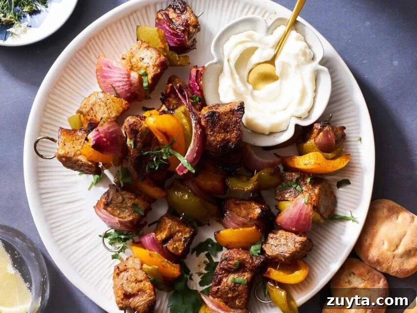 A plate of grilled steak skewers with onions and peppers and a small bowl of toum on top. 
