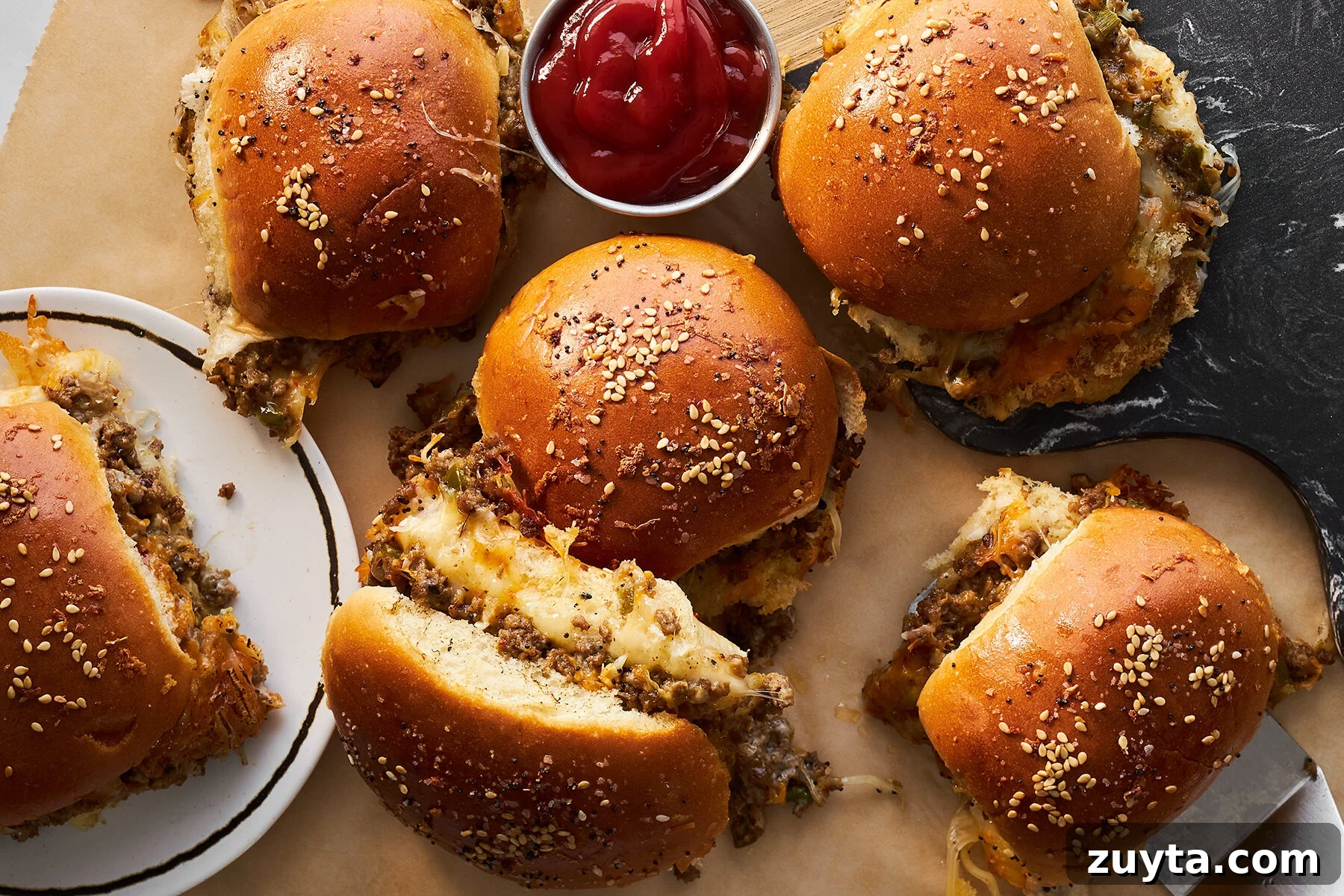 Cheesy ground beef sliders topped with sesame seeds with a small container of ketchup. 