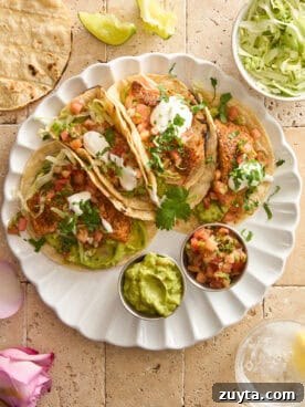 A plate of four salmon tacos with guacamole and pico de gallo.