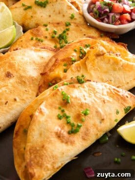A close-up of crispy tacos filled with melted cheese, garnished with chopped chives, and served with lime wedges and a small bowl of salsa on the side.