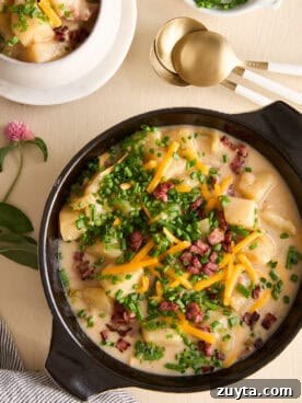 A bowl of cheesy potato soup topped with bacon, chives, and cheese.