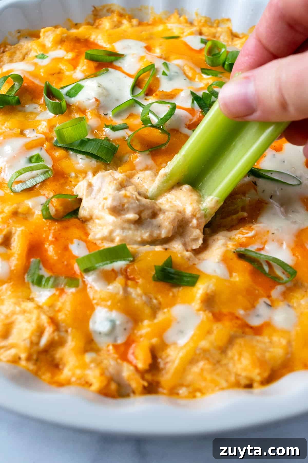 Creamy Buffalo Chicken Dip with Greek Yogurt 7 Buffalo Chicken Dip with Greek Yogurt with someone dipping a celery stick in it.