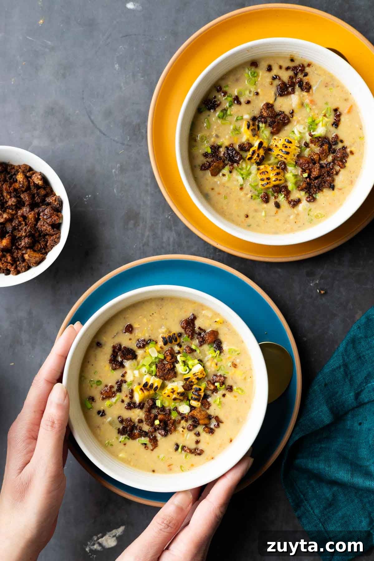 Creamy Corn Chowder with Smoky Tofu Bacon Bits 4 hands serving bowls of corn chowder