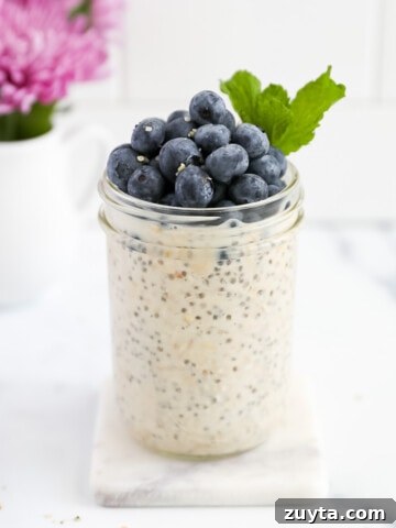 A mason jar filled with overnight oatmeal and topped with blueberries and fresh mint