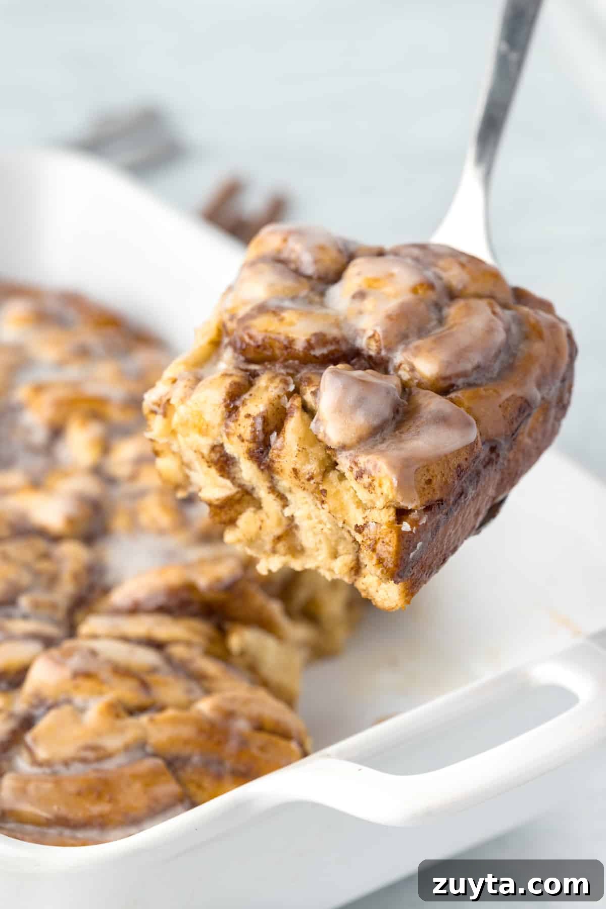 Cinnamon Roll Casserole Recipe with Cream Cheese Glaze 10 Lifting a portion of cinnamon roll breakfast bake from a baking dish.