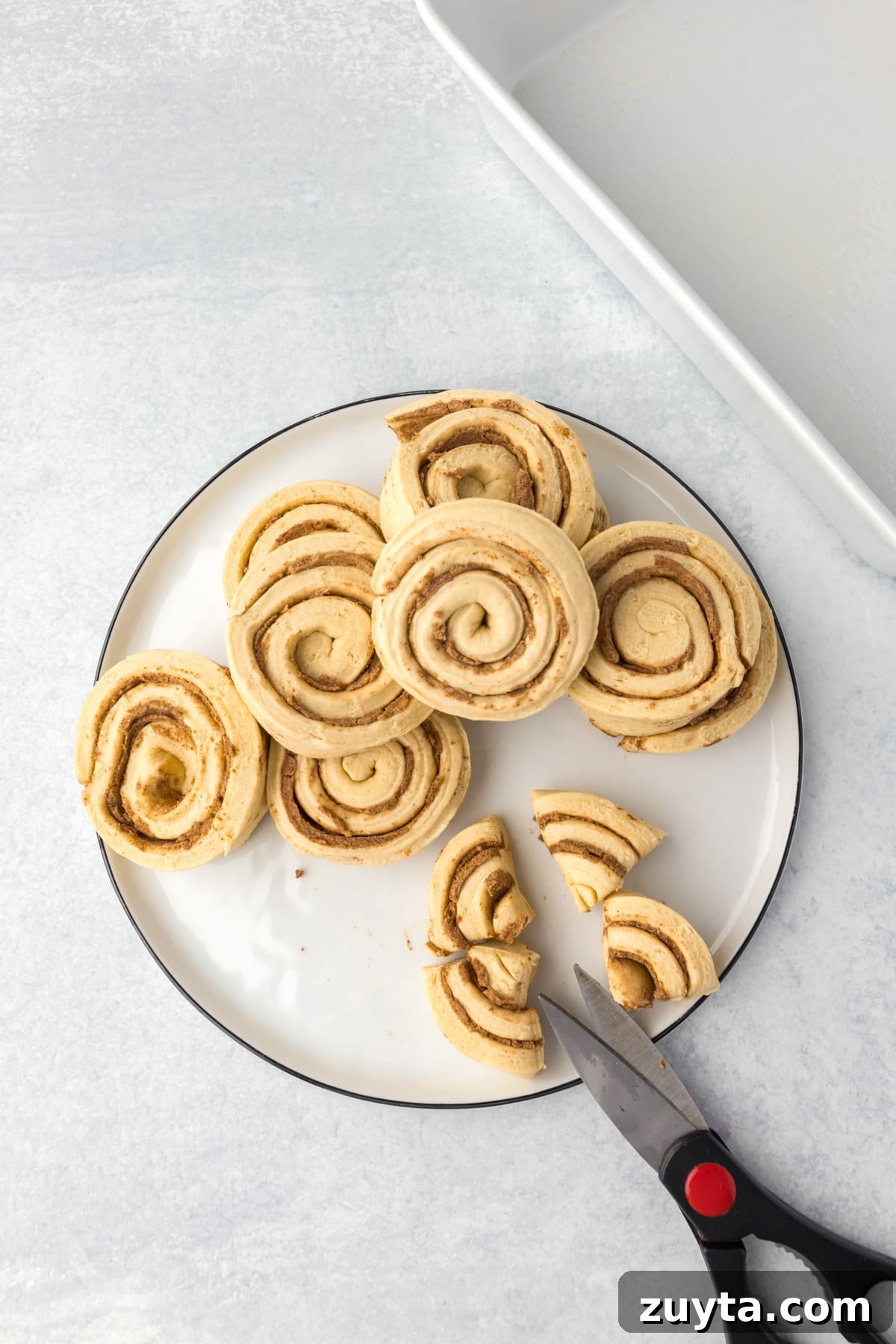 Cinnamon Roll Casserole Recipe with Cream Cheese Glaze 4 Slicing cinnamon rolls into quarters with scissors.