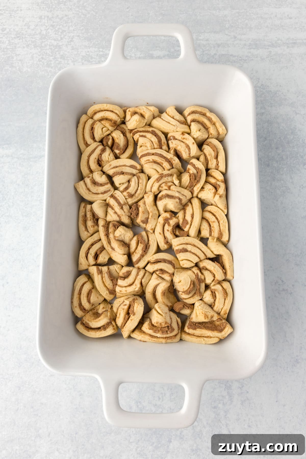 Cinnamon Roll Casserole Recipe with Cream Cheese Glaze 5 A casserole dish with cinnamon rolls sliced and fit into the dish in an even layer.