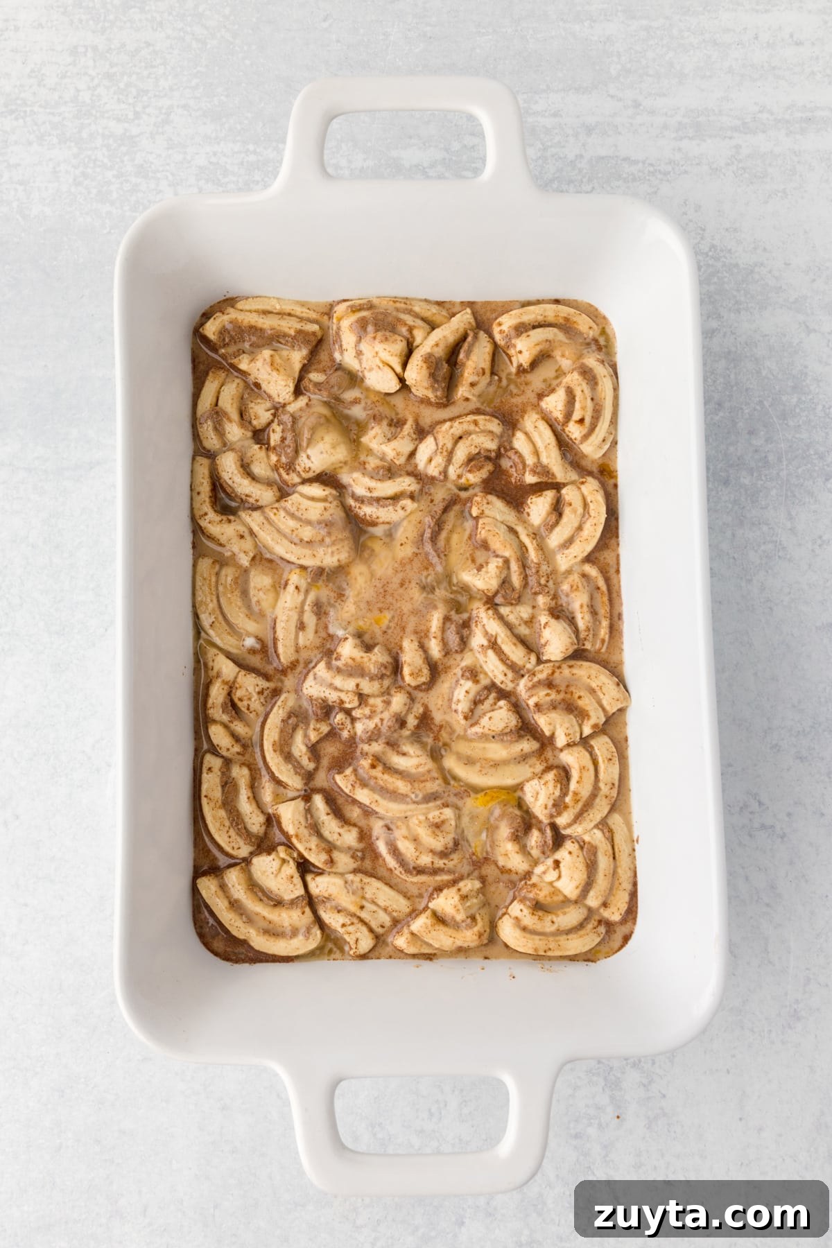 Cinnamon Roll Casserole Recipe with Cream Cheese Glaze 9 A baking dish with sliced cinnamon rolls and a custard base in it.