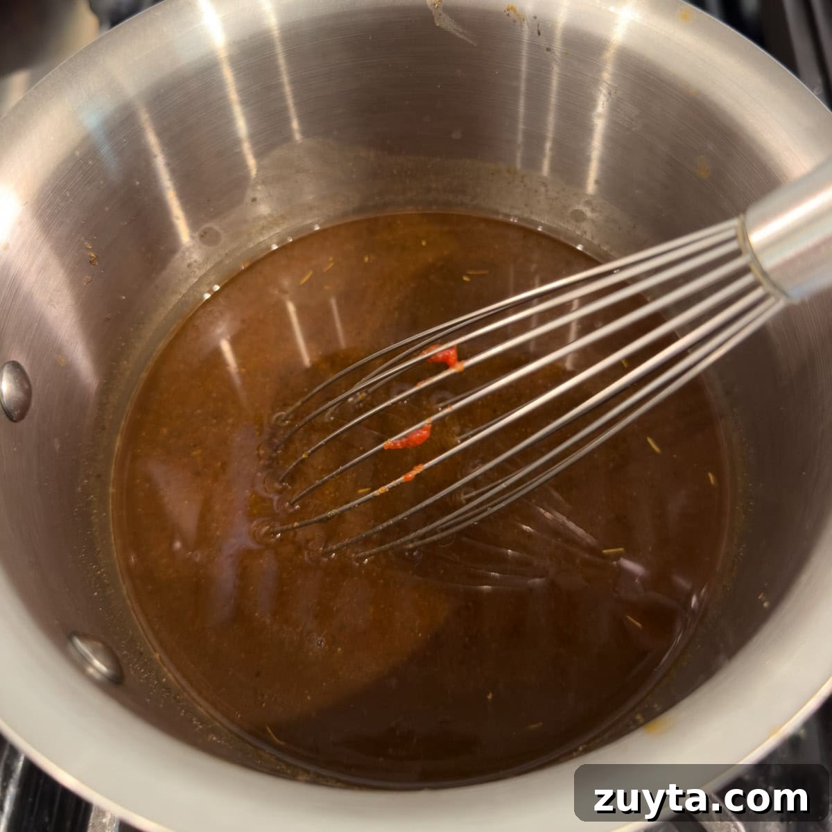 Deep brick colored red enchilada sauce with a silver whisk in a small pot.