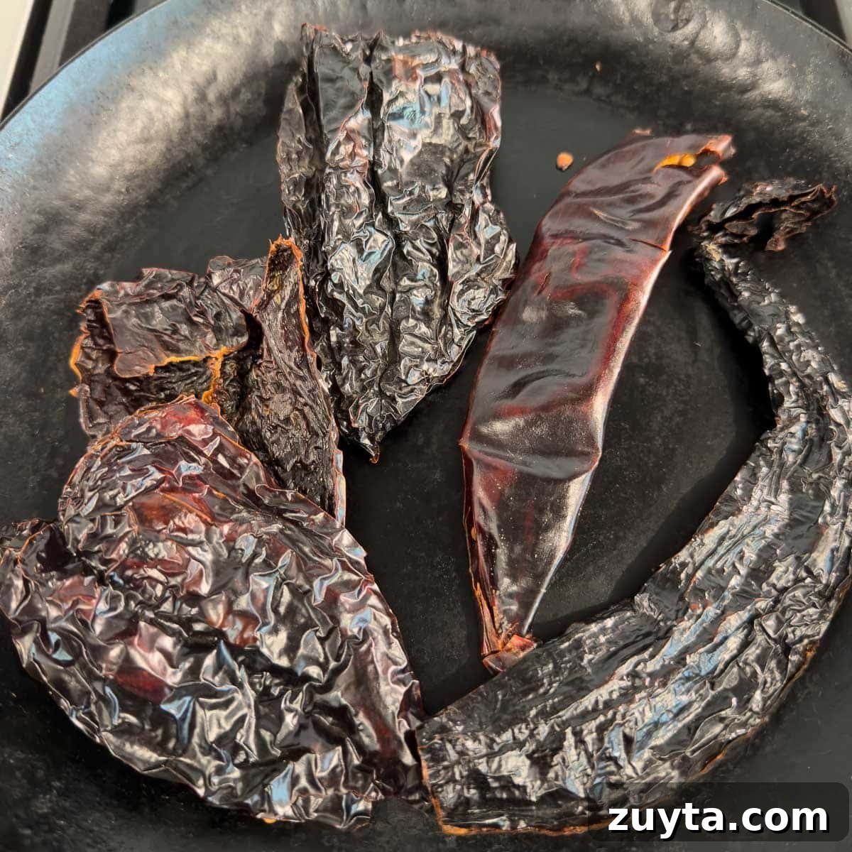 Toasting dried chili peppers in a black skillet.