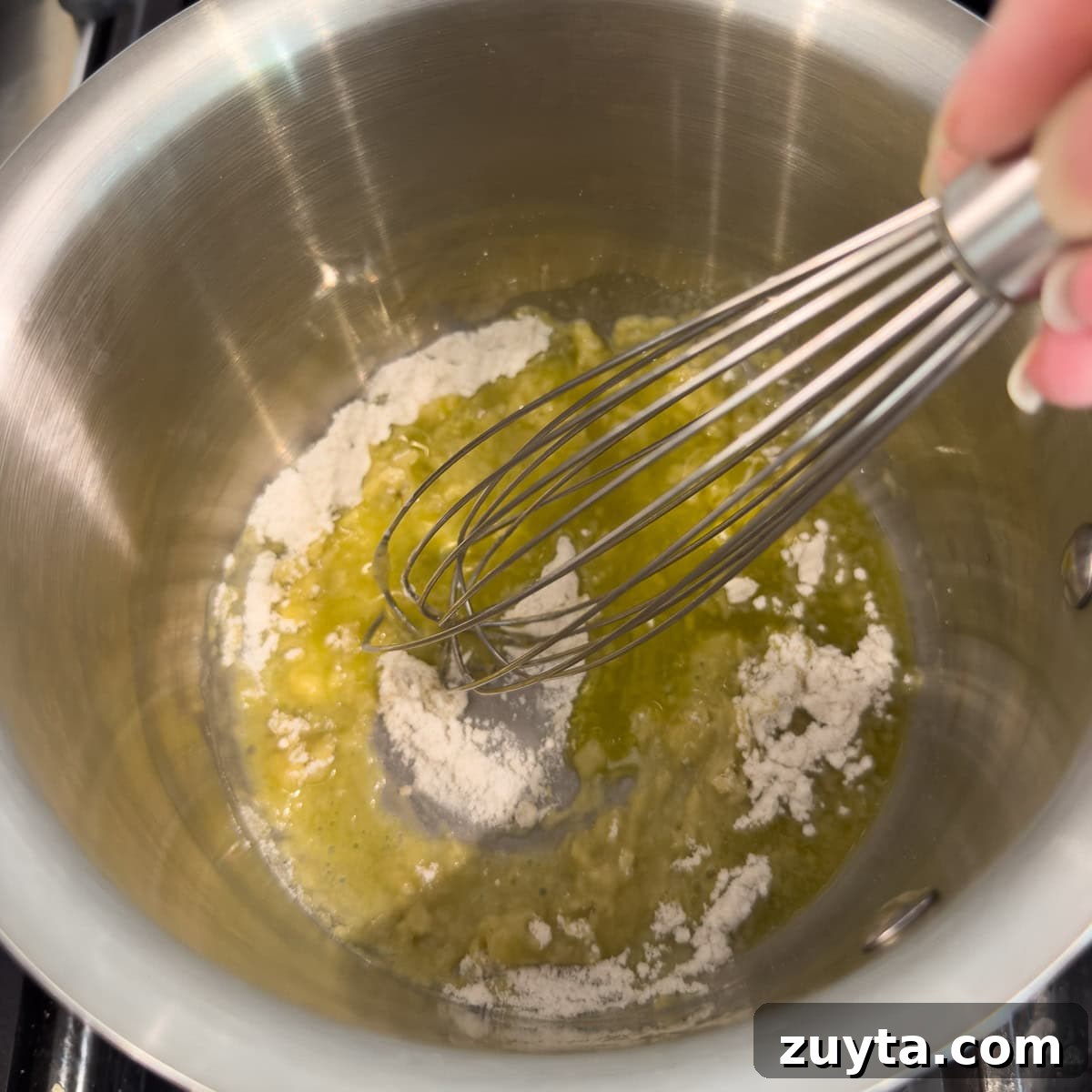 Making a roux with oil and flour to create a sauce base, with a silver whisk.