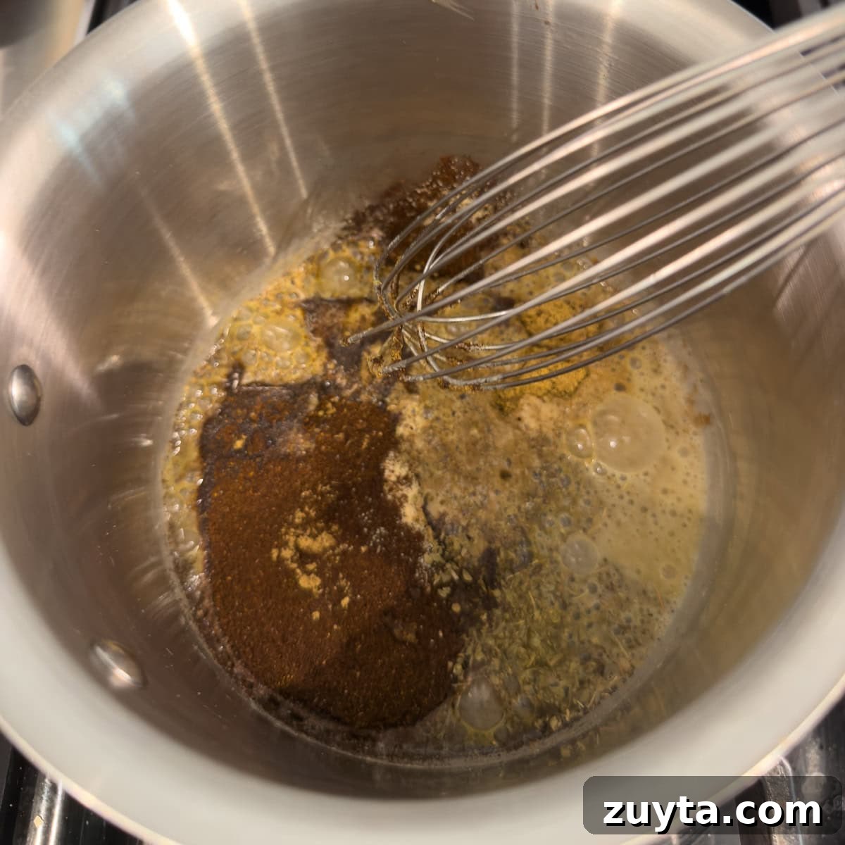 Adding spices to a small pot with a roux for making red enchilada sauce.