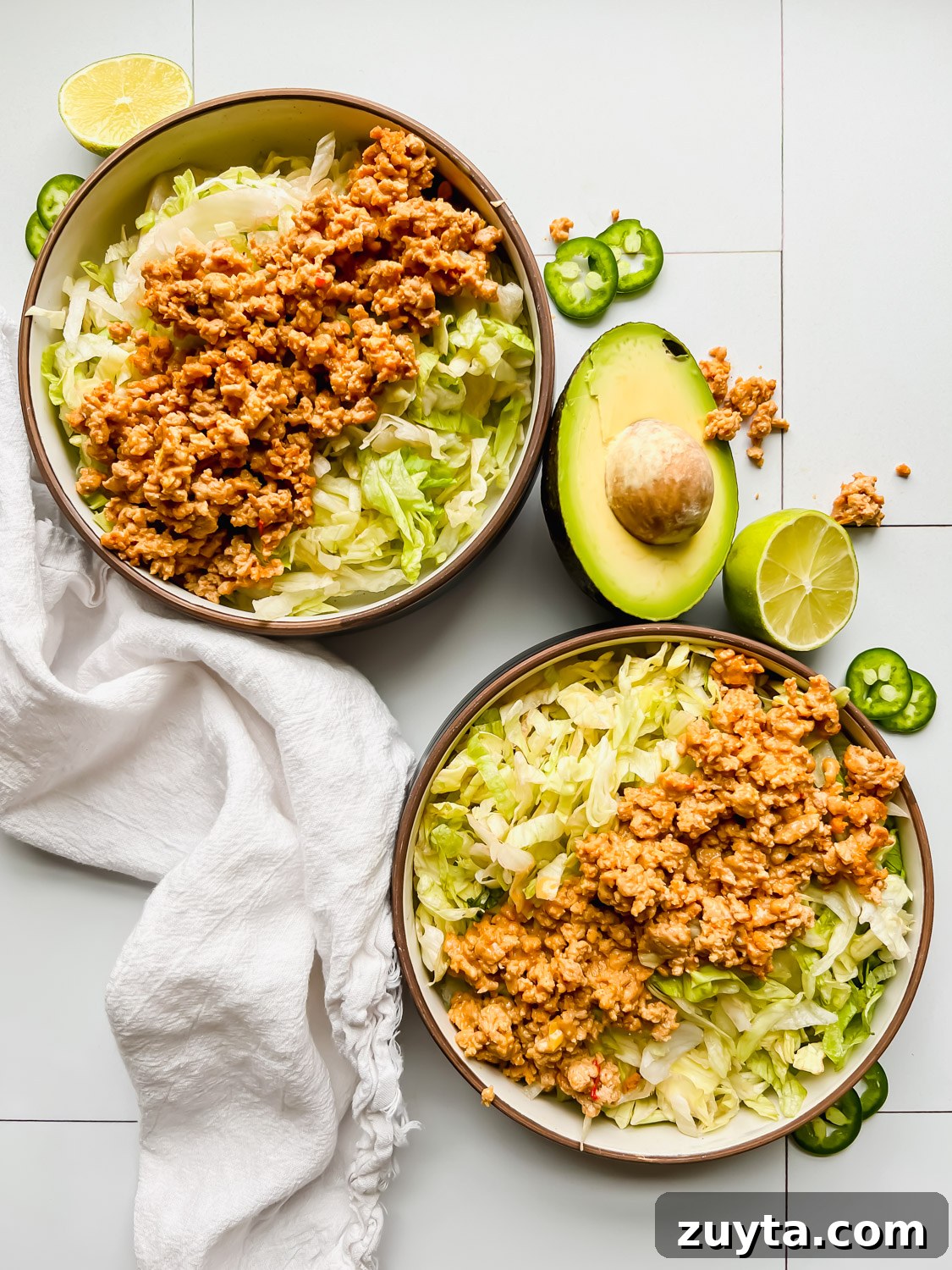 two bowls filled with lettuce and ground turkey on white tiled background