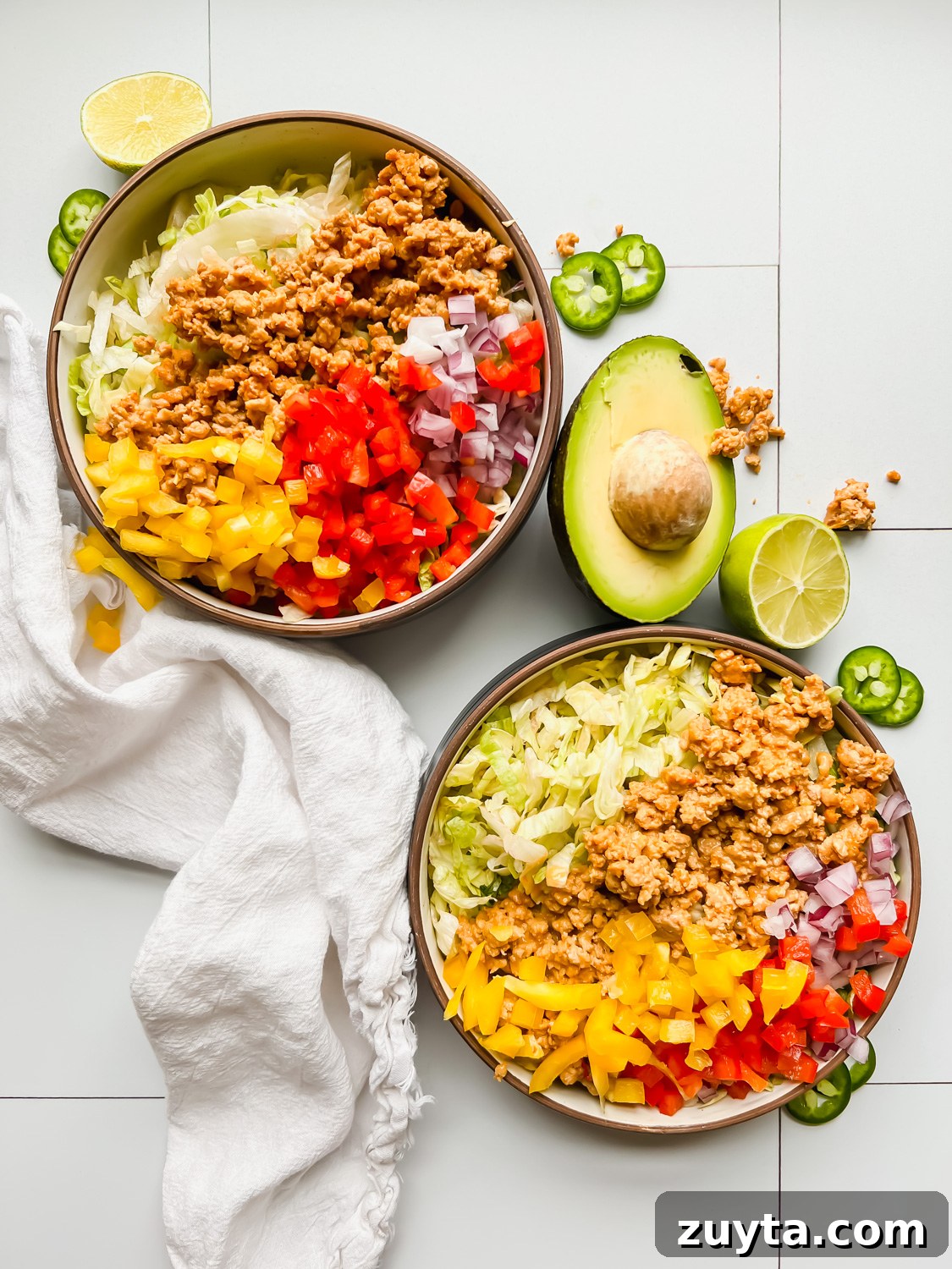 two bowls of taco salad filled with lettuce, turkey, and fresh peppers on a white tiled background