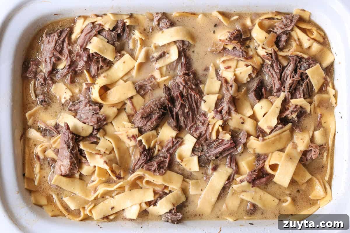 shredded beef in slow cooker with noodles and gravy