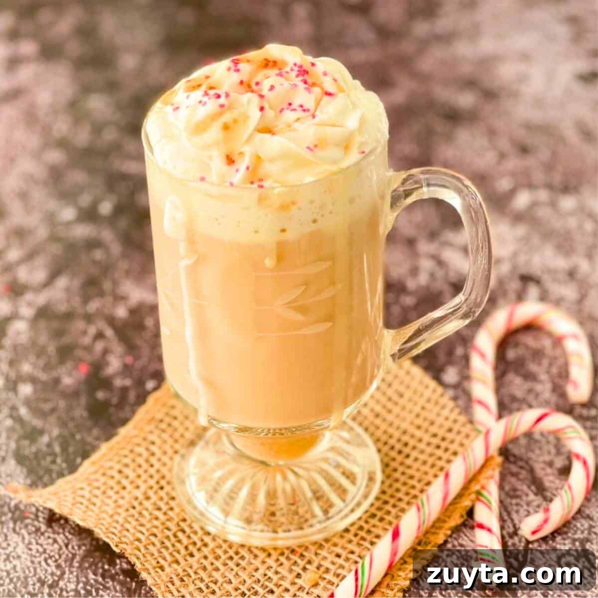 Toasted white chocolate mocha with caramel drizzle and sugar sprinkles, with two candy canes beside it.