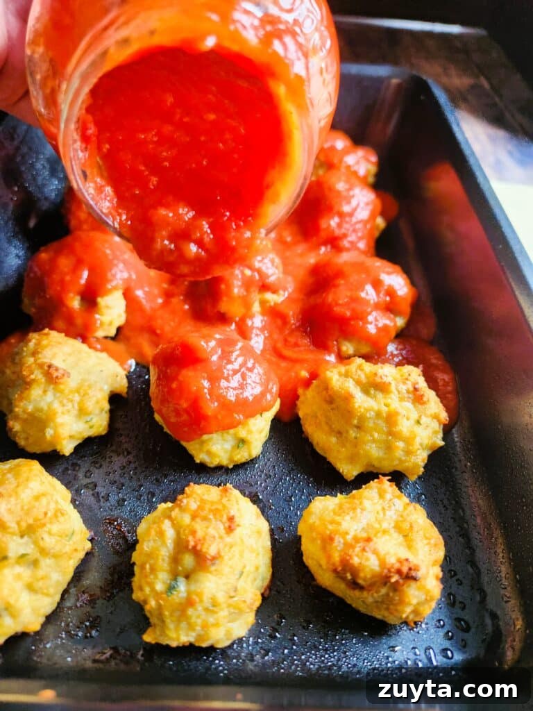 Baked Chicken Meatballs with Mozzarella in Tomato Sauce 5 Baked chicken meatballs being covered with rich tomato sauce in a baking dish