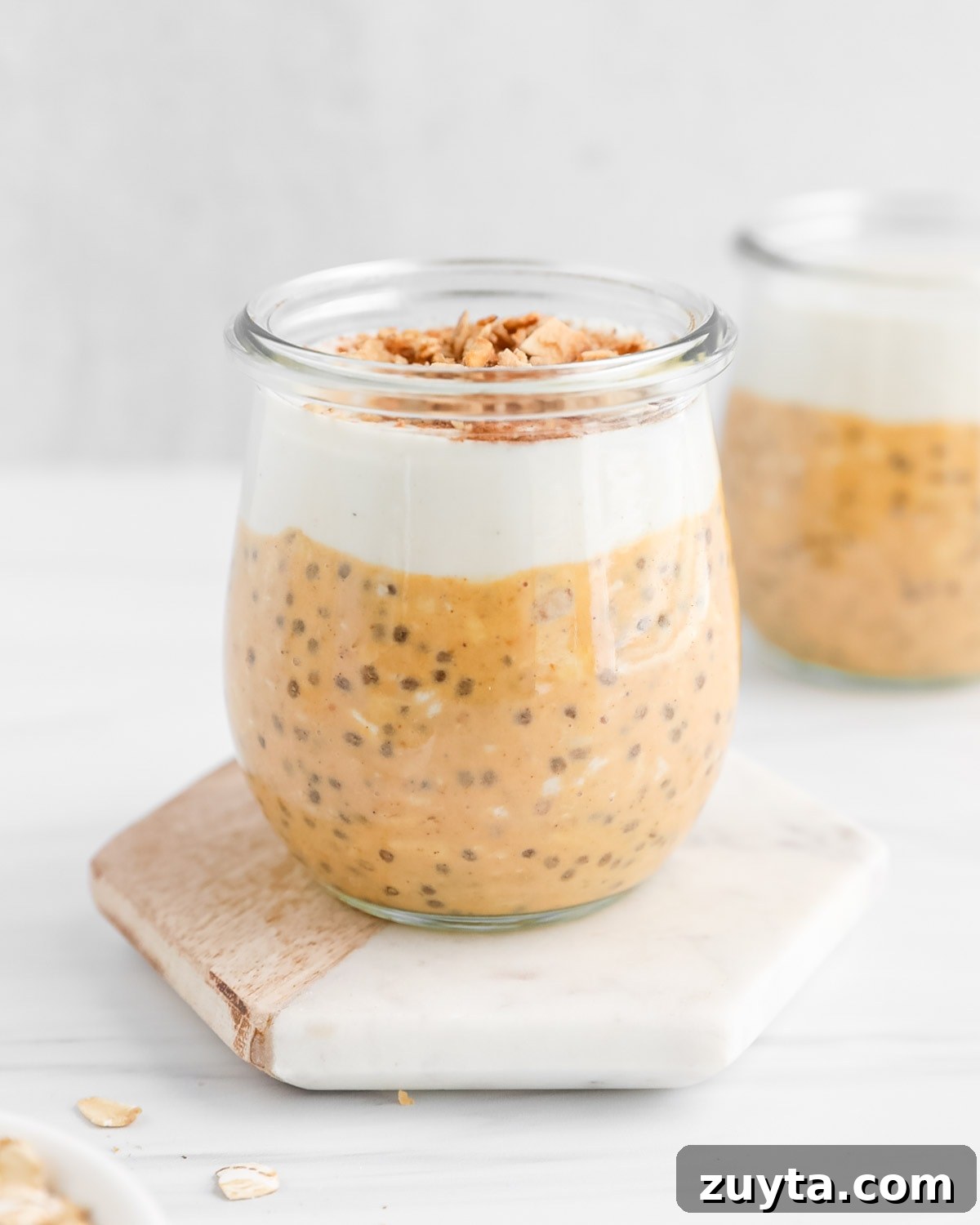 Creamy Pumpkin Pie Overnight Oats Recipe 2 A glass sitting on a coaster filled with pumpkin oats, yogurt, and granola.
